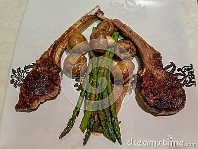 Lamb cutlets with asparagus and mushrooms with sauce, on a white ceramic plate Stock Photo