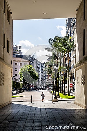 Lame disabled woman comes out of a dark courtyard onto a bright palm summer alley on a modern European city street Editorial Stock Photo