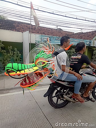 Lamongan, East Java, Indonesia. a motorcyclist carrying a kite in the shape of a green dragon's head Editorial Stock Photo