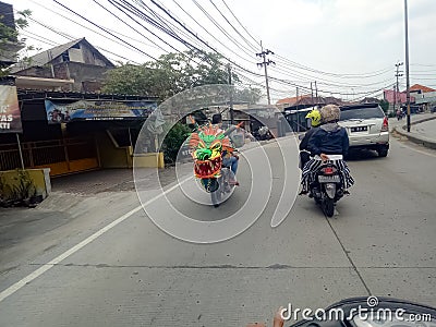 Lamongan, East Java, Indonesia. a motorcyclist carrying a kite in the shape of a green dragon's head Editorial Stock Photo