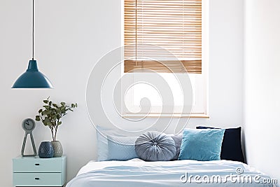 Lamp above blue cabinet with plant next to bed in simple bedroom Stock Photo