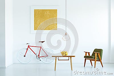 Lamp above wooden table in white flat interior with green armchair and yellow painting above bike. Real photo Stock Photo