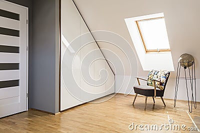 Lamp next to armchair on wooden floor in white attic interior wi Stock Photo