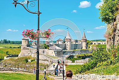 Lamppost decorated with pink flowers and walking people by Kamianets-Podilskyi fortress, selective focus Editorial Stock Photo