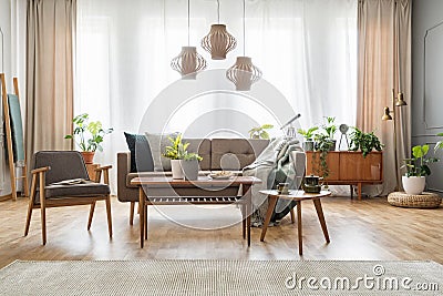 Lamps above wooden table with flowers in bright living room interior with sofa and armchair. Real photo Stock Photo