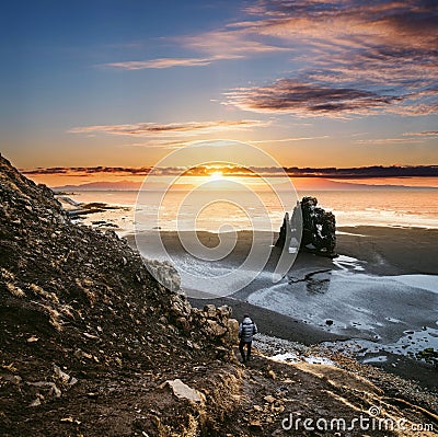 Landscape Hvitserkur in Iceland, young traveling hiking down from cliff to black sand beach in sunset Stock Photo