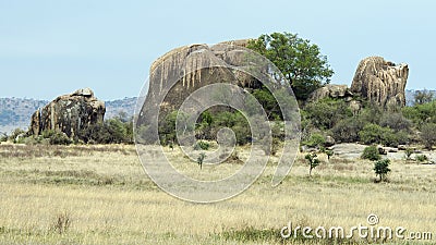 Landscape of interesting rock formation and trees surrounded by grassland with blue sky Stock Photo