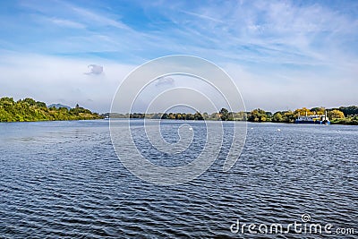 Landscape of Maas river surrounded by lush green trees against misty blue sky Stock Photo