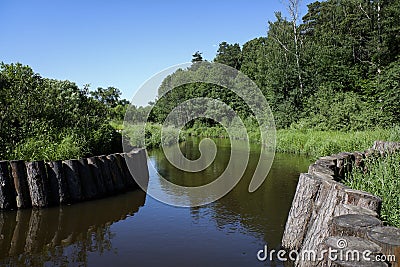 Landscape of a rivier with banks embanked with wooden logs. Sunny summer view. Stock Photo