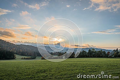 Landscape and sunset with meadow field forest tree mountains near Grafenau at Bavarian Forest with clouds and sunrays, Germany Stock Photo