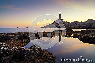 landscape view of the Botafoc Lighthouse in Ibiza Town Port at sunsetwith reflections in tidal pools in the foreground Stock Photo