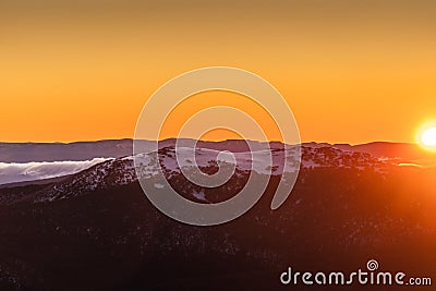 Landscape view with snowy and rocky mountain at sunset, fiery sky and sun background Stock Photo