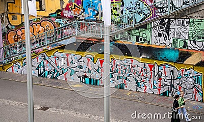 Landscape view of tourists passing graffiti & urban art lining the embankment walls of the 