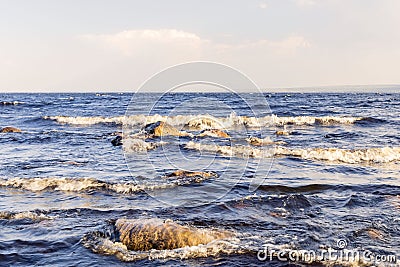 Landscape of the water surface of a large lake with stones and waves against the blue sky. Stock Photo