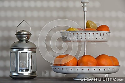 A lantern with candle next to a white fruit bowl with oranges and a lemon Stock Photo