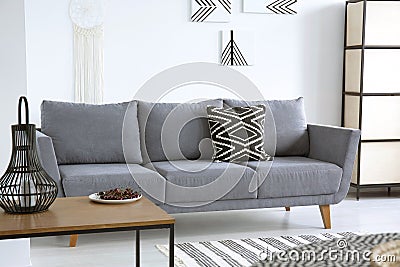 Lantern on table near grey sofa with patterned cushion in white Stock Photo