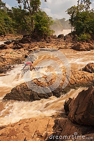 Laos fisherman in rapids of Khone Phapheng Falls on the Mekong River. The Khone Phapheng Falls are the largest in southeast asia. Editorial Stock Photo
