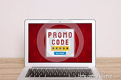 Laptop with activated promo code on wooden table near white wall Stock Photo