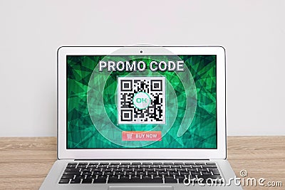 Laptop with activated promo code on wooden table near white wall Stock Photo