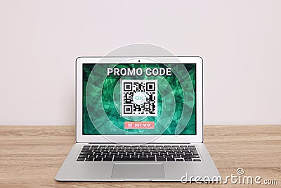 Laptop with activated promo code on wooden table near white wall Stock Photo