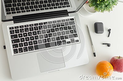 Laptop, black wireless earbuds, pen, potted plant, apple and orange isolated on white background Editorial Stock Photo