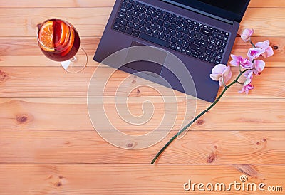 Laptop, branch of orchid and glass of sangria on wooden table Stock Photo