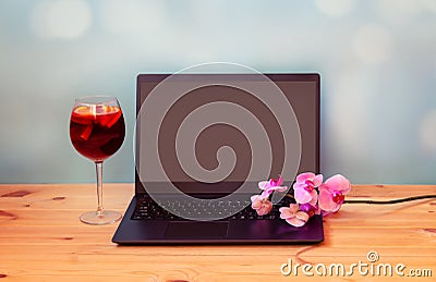 Laptop, branch of orchid and glass of sangria on wooden table Stock Photo