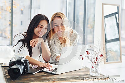 With laptop and camera. Two young female freelancers working indoors in the office at daytime Stock Photo
