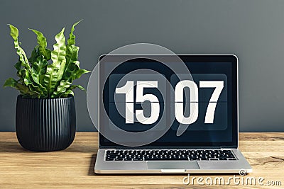 Laptop with clock screensaver placed on wooden desk with fresh green potted plant Stock Photo