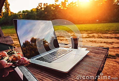 Laptop computer on rough wooden table with coffee cup and bouquet of peonies flowers in outdoor park Stock Photo