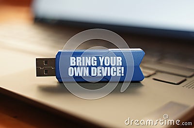 On the laptop keyboard is a flash drive with the inscription - BRING YOUR OWN DEVICE Stock Photo