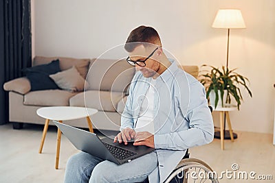 With laptop on the legs. Disabled man in wheelchair is at home Stock Photo