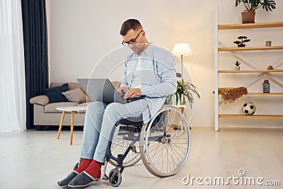 With laptop on the legs. Disabled man in wheelchair is at home Stock Photo