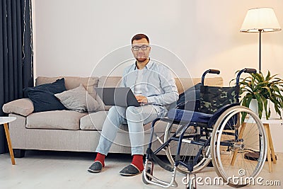 With laptop on the legs. Disabled man in wheelchair is at home Stock Photo