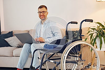 With laptop on the legs. Disabled man in wheelchair is at home Stock Photo