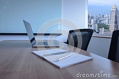 Laptop and pen on notepad for agenda kept on table in empty corporate conference room with cityscape view on background. Stock Photo