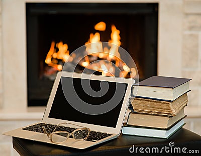 Laptop and pile of books against the background of the fireplace Stock Photo