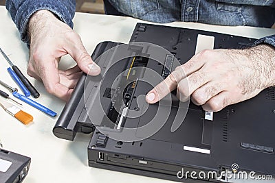 Laptop service. Removal of the battery by a service technician. Tools lie on the table next to Stock Photo