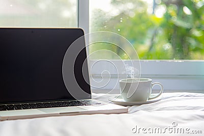 The laptop working on the white bed and coffee in the window on rainy day, Fresh morning holiday. Stock Photo