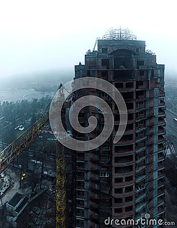 abandoned unfinished brick building skyscraper and big yellow machine crane Stock Photo