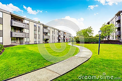 Large beige apartment building with three floors and balconies. Well kept lawn Stock Photo