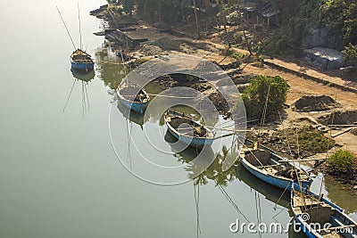 Large blue fishing boats on the shore on the smooth water against the green jungle and huts Stock Photo