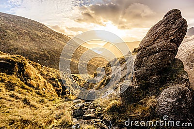 Large boulder and valley with water reservoir, dramatic sunset with sunrays. Mourne Mountains Stock Photo