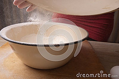 Large bowl, cutting board, sieve for sifting flour on the table. Female hands sifting flour in the home kitchen Stock Photo