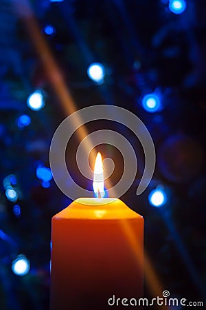 A large candle burns against the background of a garland with shining lights. Vertical photo, defocus. Mystic esoteric romance Stock Photo