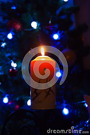 A large candle burns against the background of a garland with shining lights. Vertical photo, defocus. Mystic esoteric romance Stock Photo