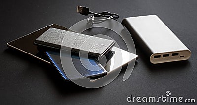 A large and capacious external battery - power bank with three line outputs lies next to three gadgets: a tablet and two Stock Photo