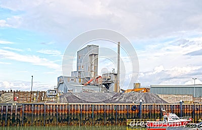 A cement works in with the a boat on the sea in front . Editorial Stock Photo