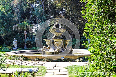A large circular fountain with fish head sculptures in the garden surrounded by lush green trees at Huntington Library and Botanic Stock Photo