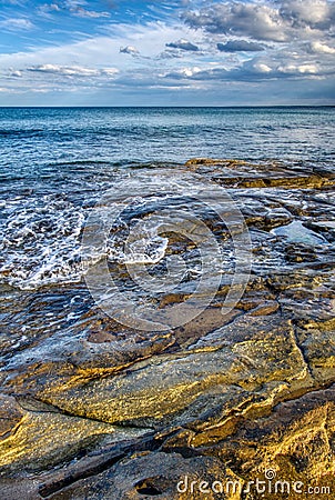 Large colourful rocks just under the surface, sea water soft waves blue sky with clouds Stock Photo